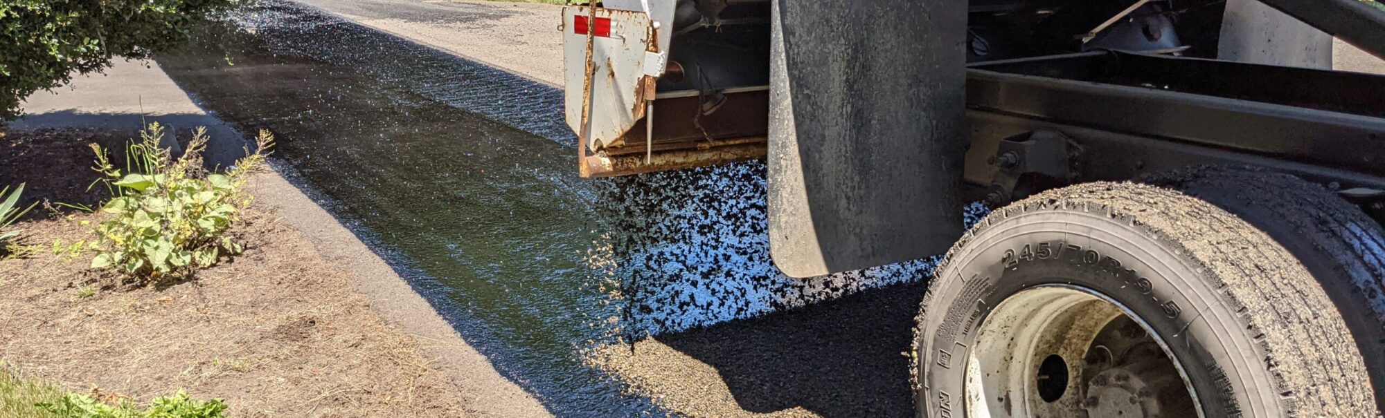 Chip seal rock being applied to fresh chip oil